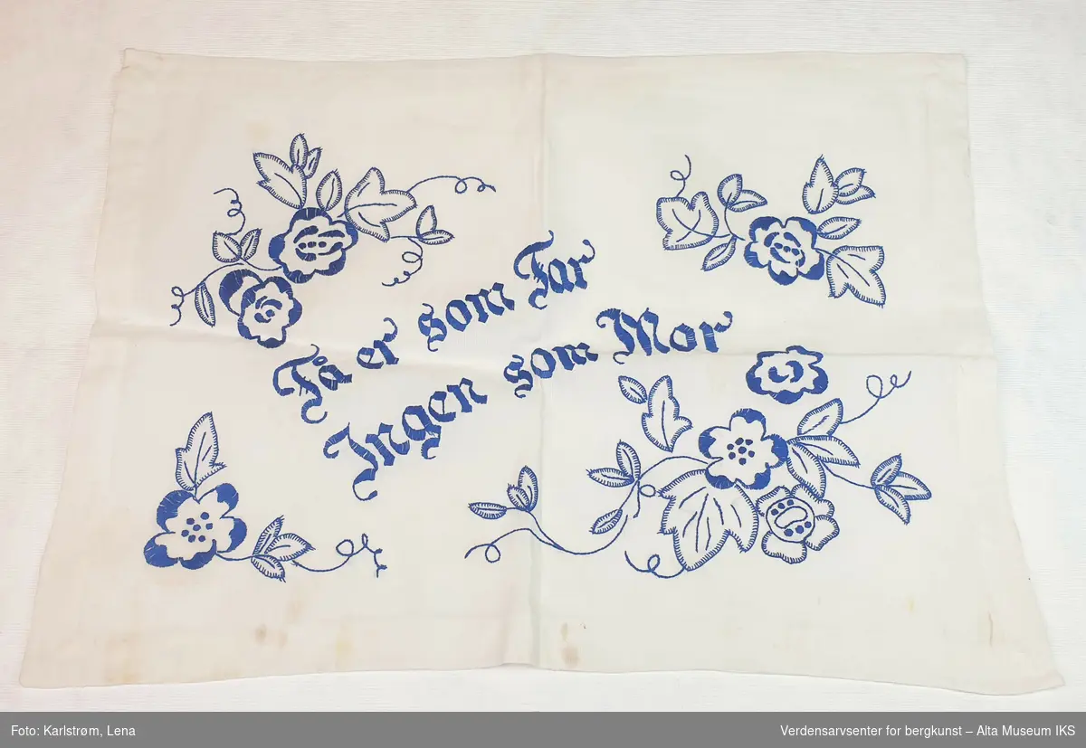 Håndsydd duk i hvitt bomullstøy med blå broderte blomster og teksten: "Få er som far, ingen som mor".