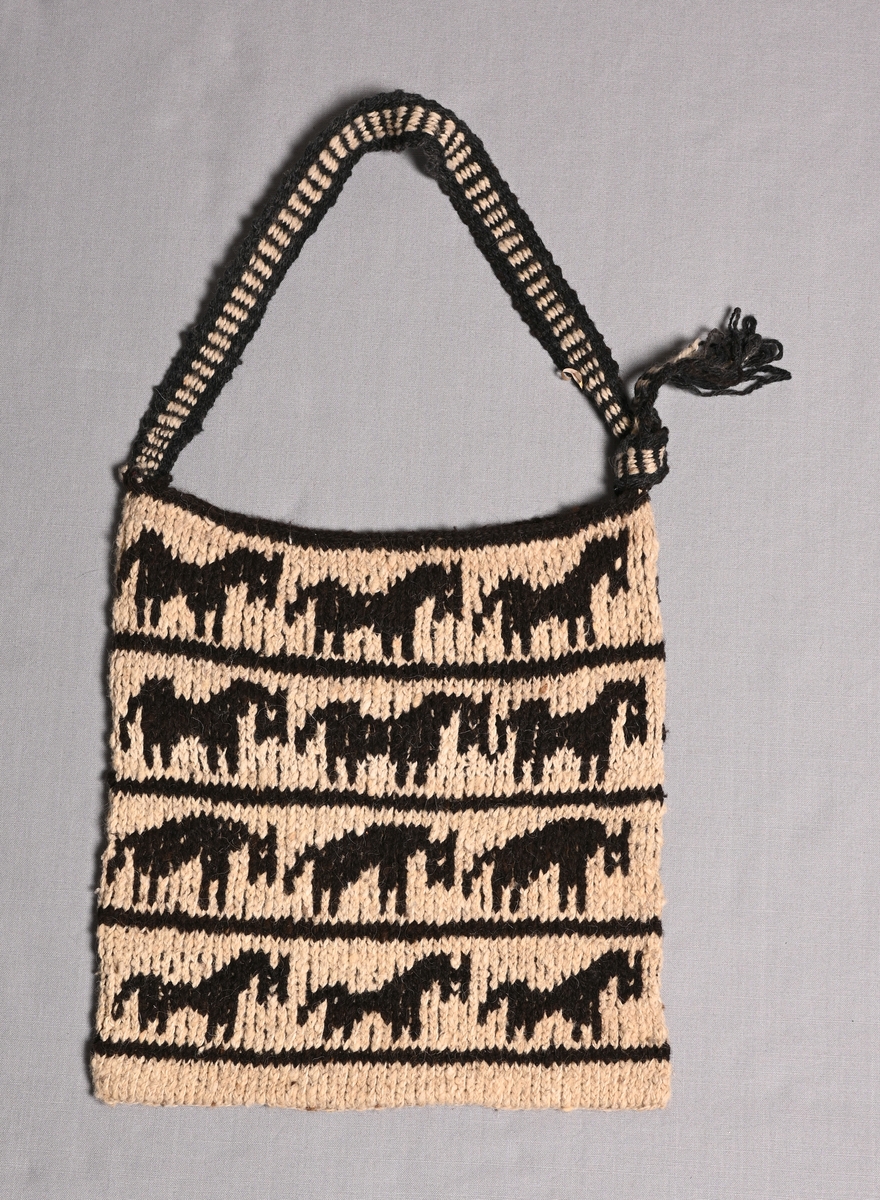 Stickad väska från Guatemala.
Mönsterstickad i naturvit och naturbrun 2-trådig lamaull med hästliknande djur i tre rader. Vävt tuskaftsband som bärrem i samma färger.