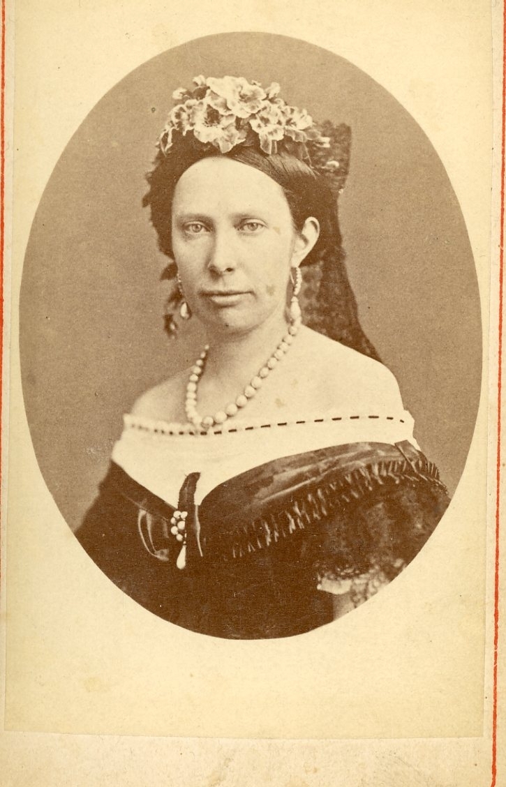 Kabinettsfotografi av en kvinna med blommor i uppsatt hår och halsband.