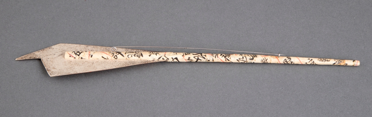 Brosje bestående av en spisepinne i bambus dekket med japansk papir med skrifttegn på. På den øvre delen er det festet en uregelmessig sølvplate med pålagt gullfolie. Denne platen en tilnærmet pilespissformet. Lang nål på baksiden.