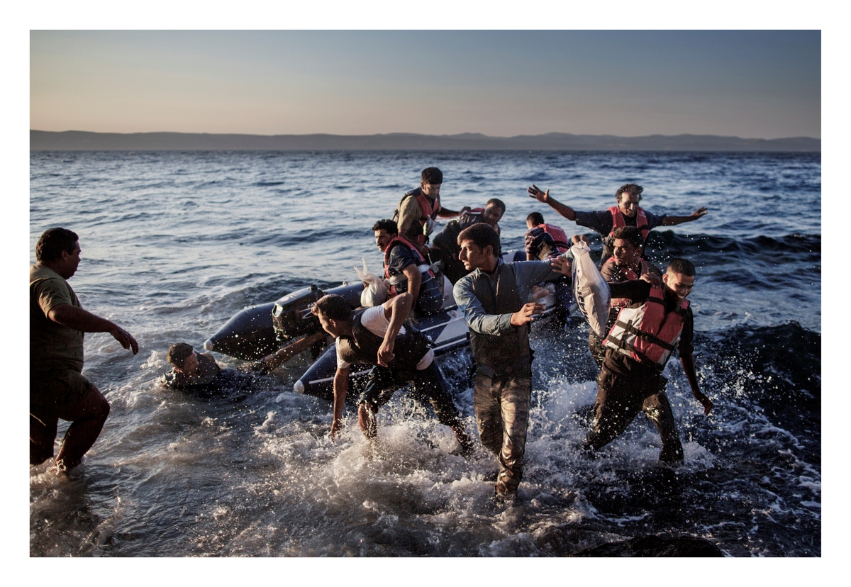 Syriske flyktninger hopper ut av gummibåten som har tatt dem over havet som skiller Hellas fra Tyrkia. Hver dag ankom rundt 2.000 flyktninger den lille øya Lesvos. Ofte ble de møtt av mange frivillige som ga de mat og hjalp dem med informasjon om veien videre. Hver dag gikk lange rekker med flyktninger langs de smale veiene på øya mot hovedstaden, hvor de ble innkvartert i en flyktningleir før de fikk reise videre med ferger til fastlandet og Athen.