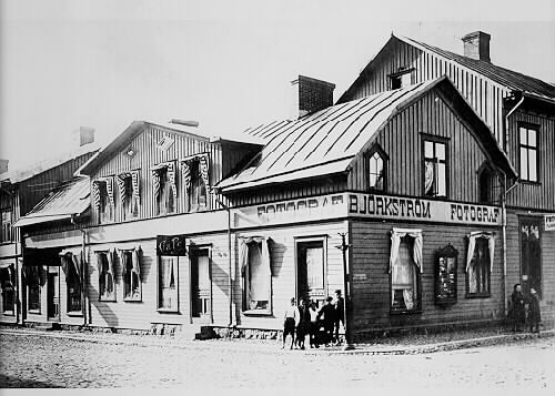 Fotograf Gustaf Björkströms ateljé och bostad på ovanvåningen i huset på hörnet Torggatan-Östra Långgatan. På gaveln sitter hans skyltskåp och till höger om det finns ingången. Han tog över ateljén 1906. I bottenvåningen ligger ett café. Ett gäng gossar står vid husknuten och ett par flickor vid Björkströms entré.
