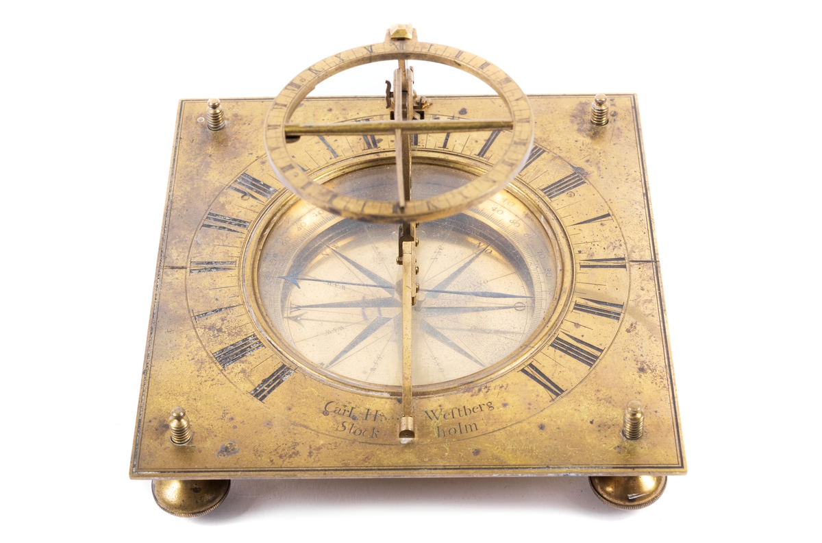 Solur med ställbar latitudbåge med skuggpinne och timcirkel samt ett mindre upphängt lod. Stativets platta har fyra skruvfötter. Ring angivande timmar graverade runt en glastäckt kompass.
Tillverkare Westber, Carl Hindric, 1720-1769