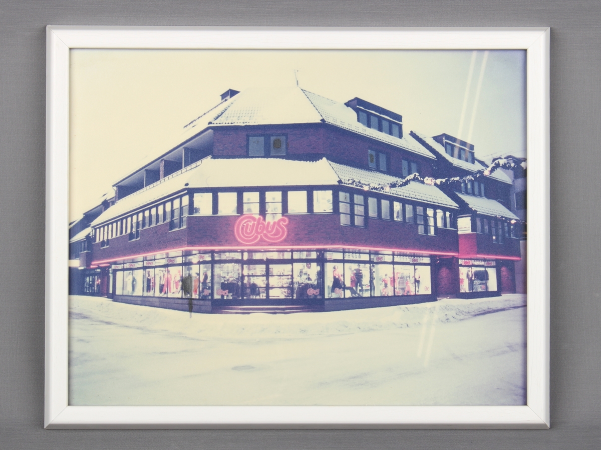 Reklameplakat i ramme, som viser fasaden til en Cubus-butikk i vinterlandskap.