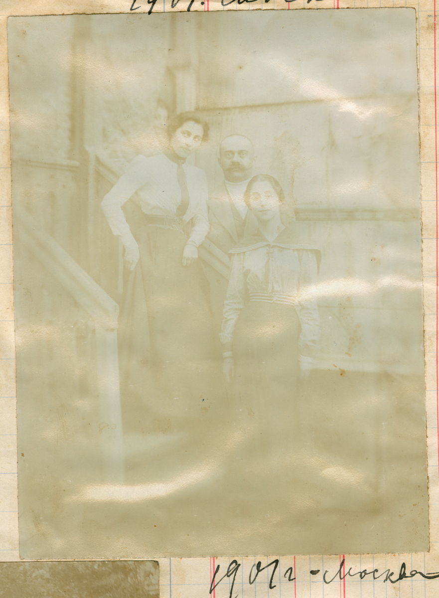 Gruppefoto av tre personer stående i en trapp, fra venstre: Florentine, onkel Heliodor Rostin og Valentine, fotografert i Moskva. I vinduet bak dem halve ansiktet til et barn som vises bak en gardin.