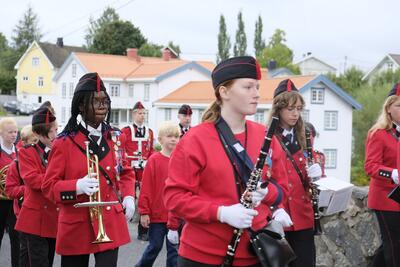 Halvnært bilde av ungdommer som marsjerer i korps iført rød uniform med svarte luer. De bærer instrumenter.