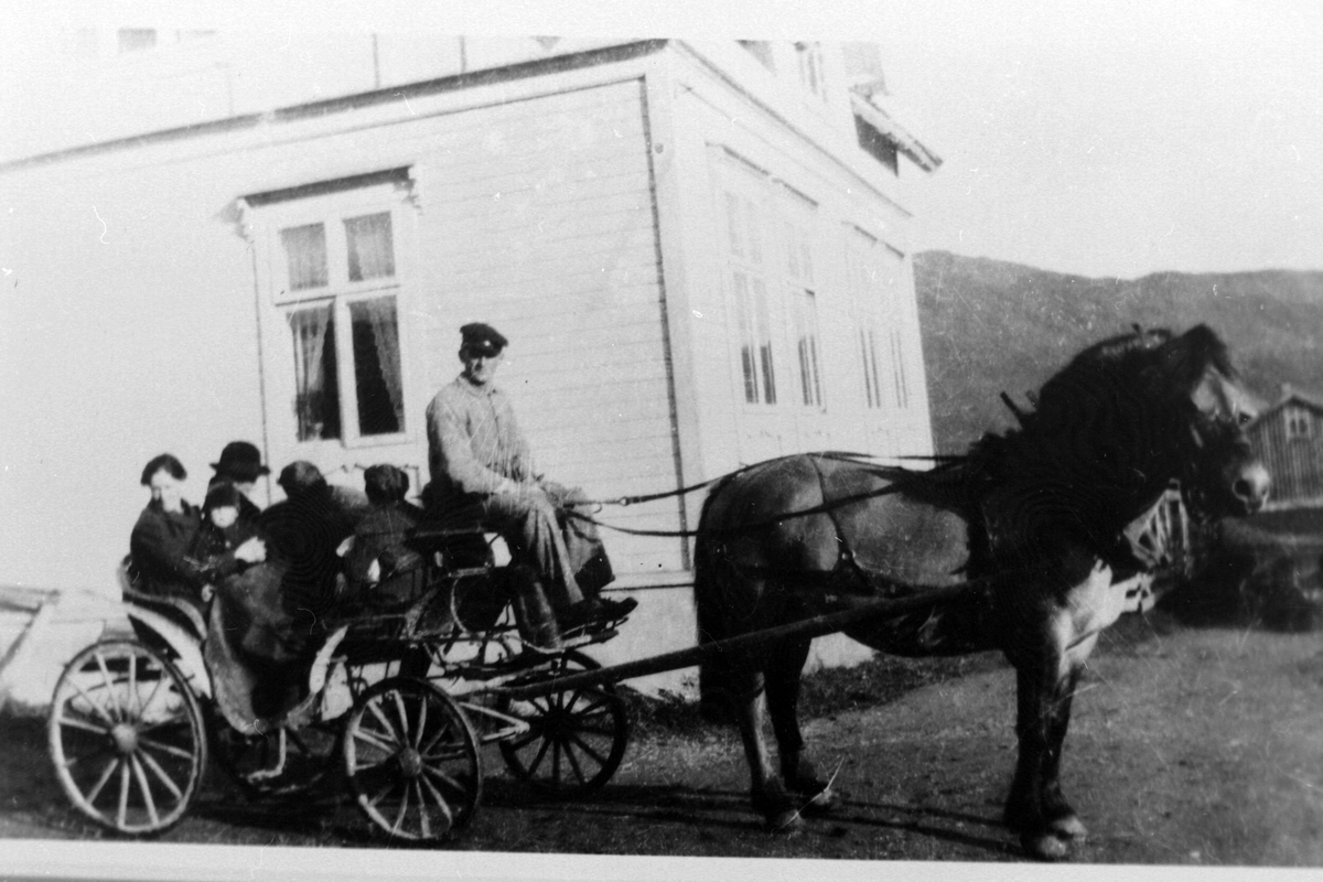 Hest med karjol på gårdstun i Kasfjord. Kusk og passasjerer på vogna.
