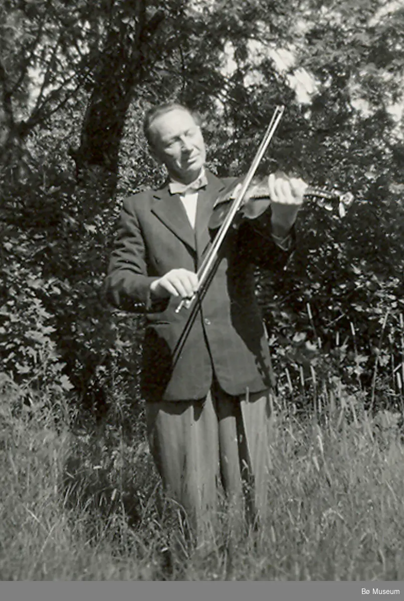 Jon Lunden (1903-1988) frå Bø spelar hardingfele ute i ein hage.