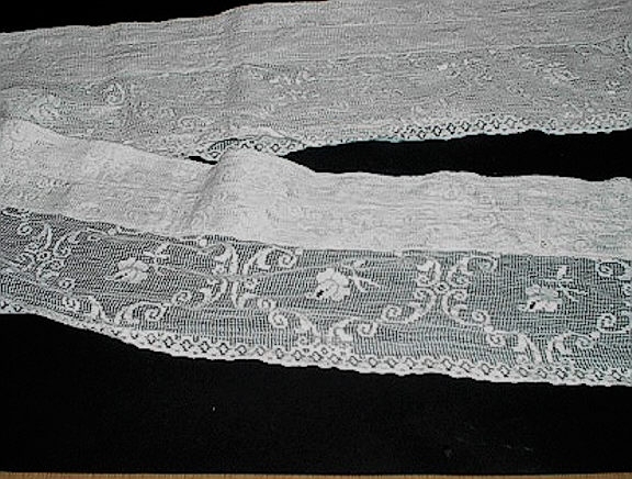 Mønstervevd gardinkappe. Rektangulært stykke med blondekant på eine langsida. Dei andre sidene er falda og sydd på maskin.