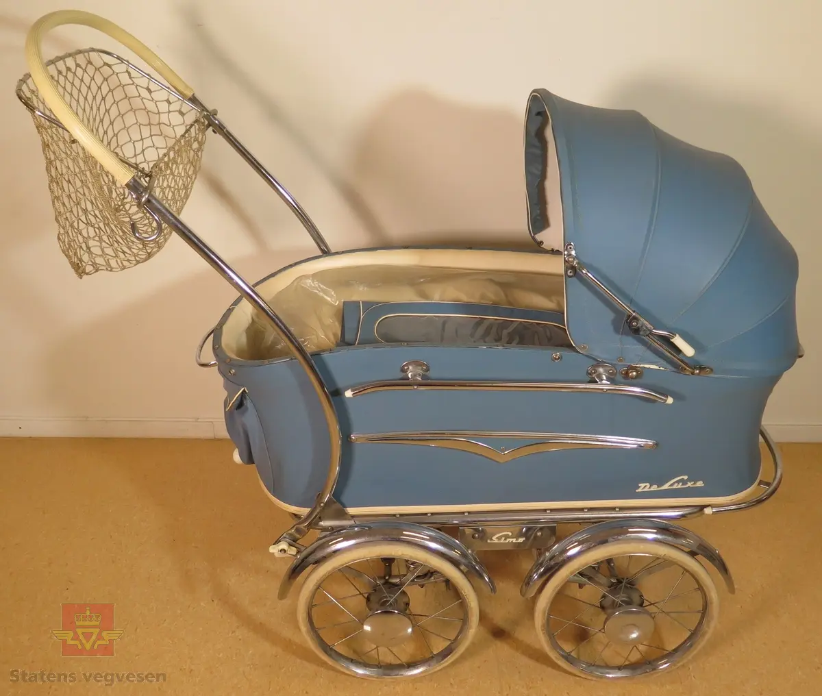Barnevogn, 2-akslet med totalt fire hjul. Hjulene har kompaktgummi. Vogna er blå med hvite og forniklede detaljer. Trekk, madrass og dyne føger med.