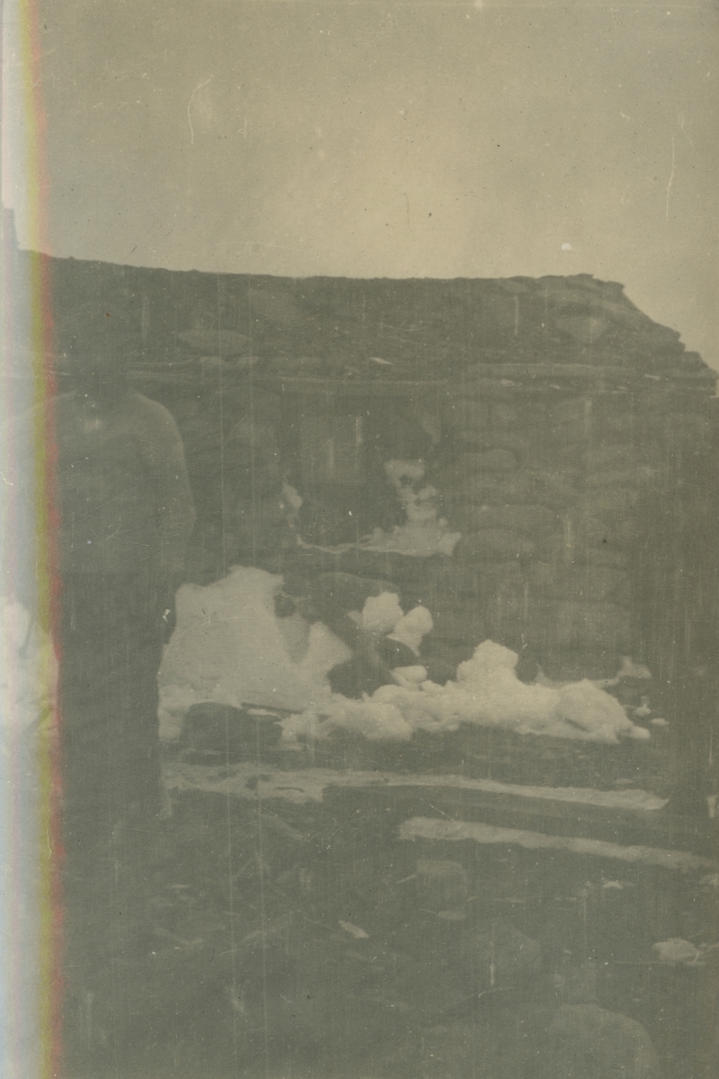 Fotografi från expedition till Spetsbergen. Motiv av pojke som står framför ett stenhus.