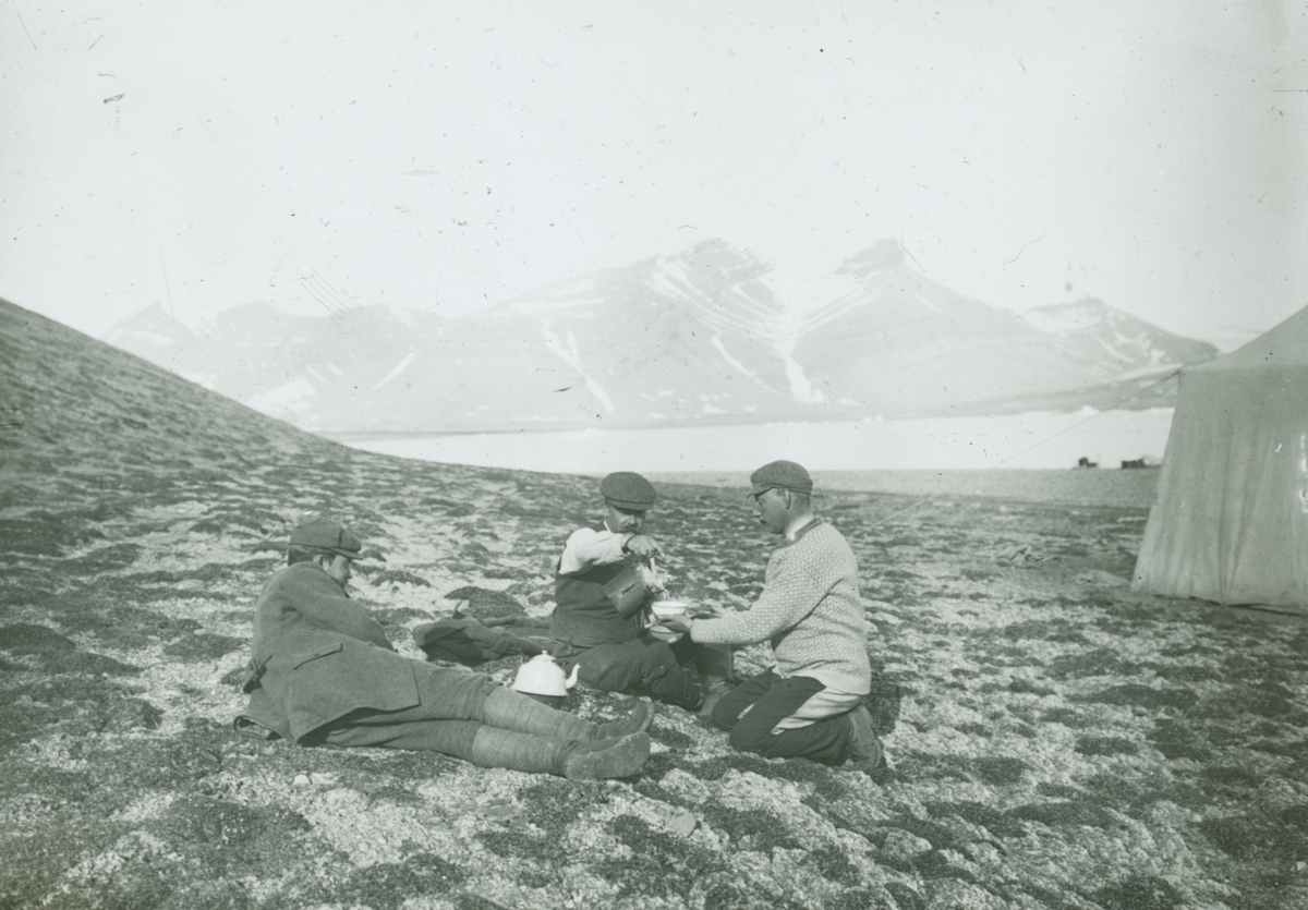 Fotografi från expedition till Spetsbergen. Motiv av tre män som dricker kaffe i bergslandskap.