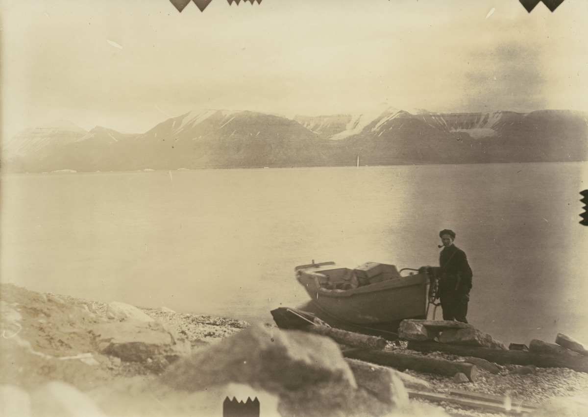 Fotografi från expedition till Spetsbergen 1920. Motiv av man med liten båt på strand vid vatten.