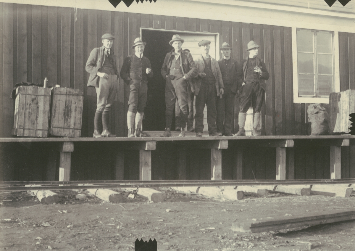 Fotografi från expedition till Spetsbergen 1920. Motiv av sex män utanför trähus.