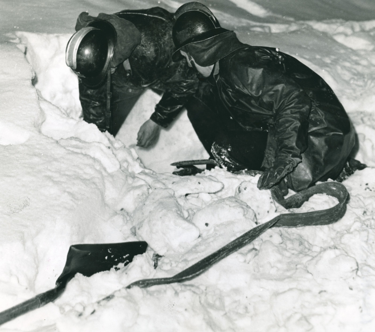 To brannmenn graver i snøen.
