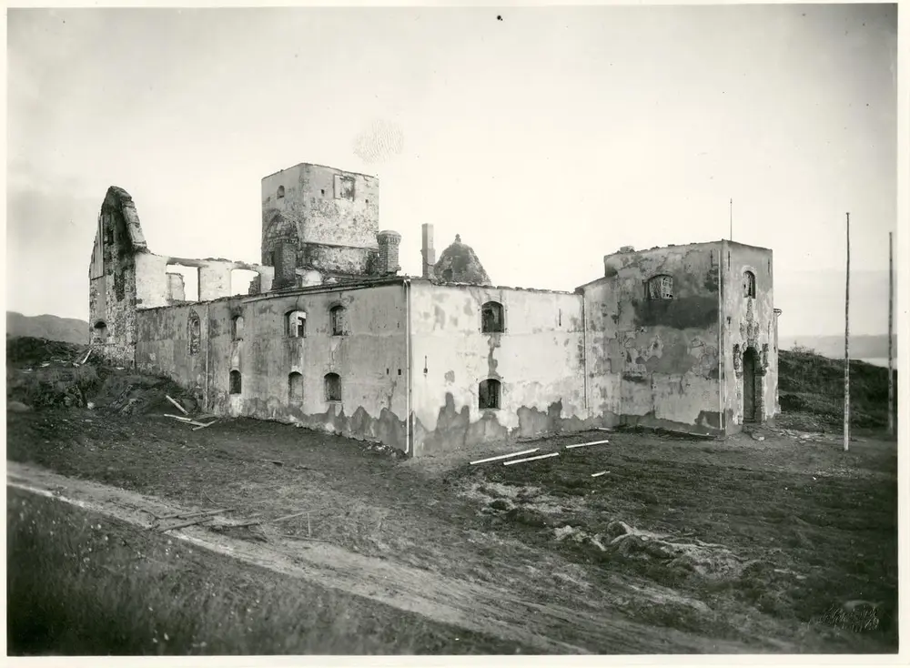 Svart-hvitt foto av brannruinen av Austråttborgen. Taket er brent opp. Muren står igjen, delvis sotete, med tomme vinduer.