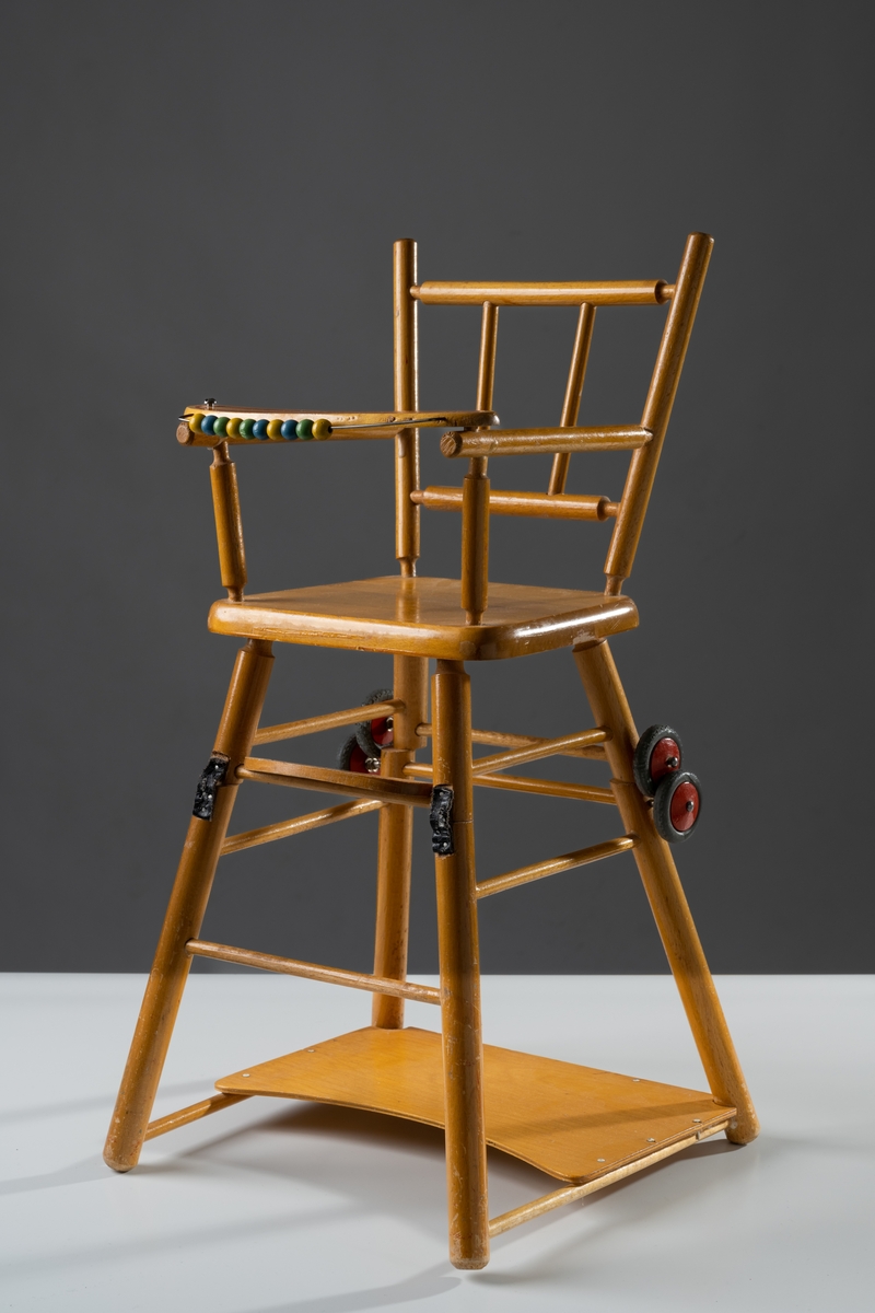Barnstol till docka av naturfärgat och lackat trä. Stolen är delbar, kan dels vara hög (matstol), dels fällas ner till stol och bord, som går att rulla (lekstol). Pinnstolsmodell med svarvade pinnar i ryggstödet och armstöden samt fyrkantig sits. Framtill sitter en smal skiva med tio målade träkulor uppträdda på en metalltråd. Skivan går att fälla upp och ut. De fyra hjulen är av trä och gummi (har torkat).

Se vidare Historik