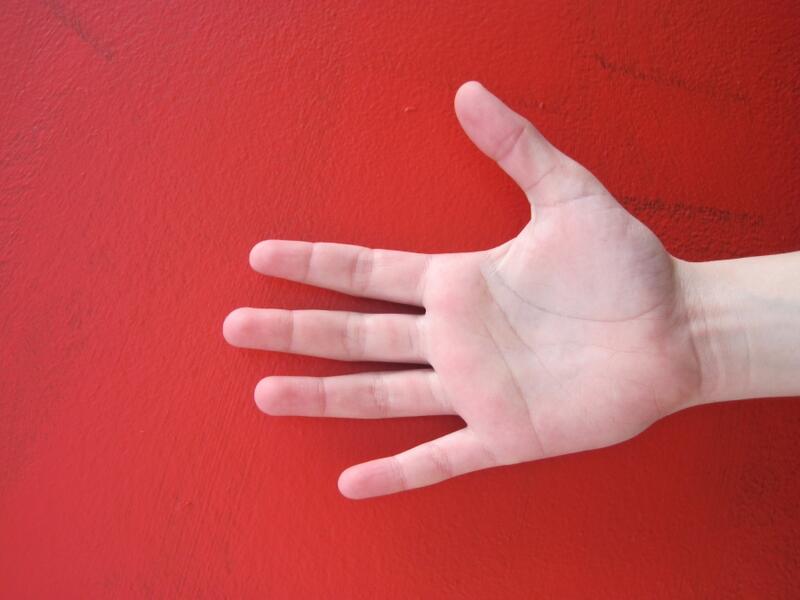 En åpen hånd med håndflaten opp mot en rød bakgrunn. Fotografi.