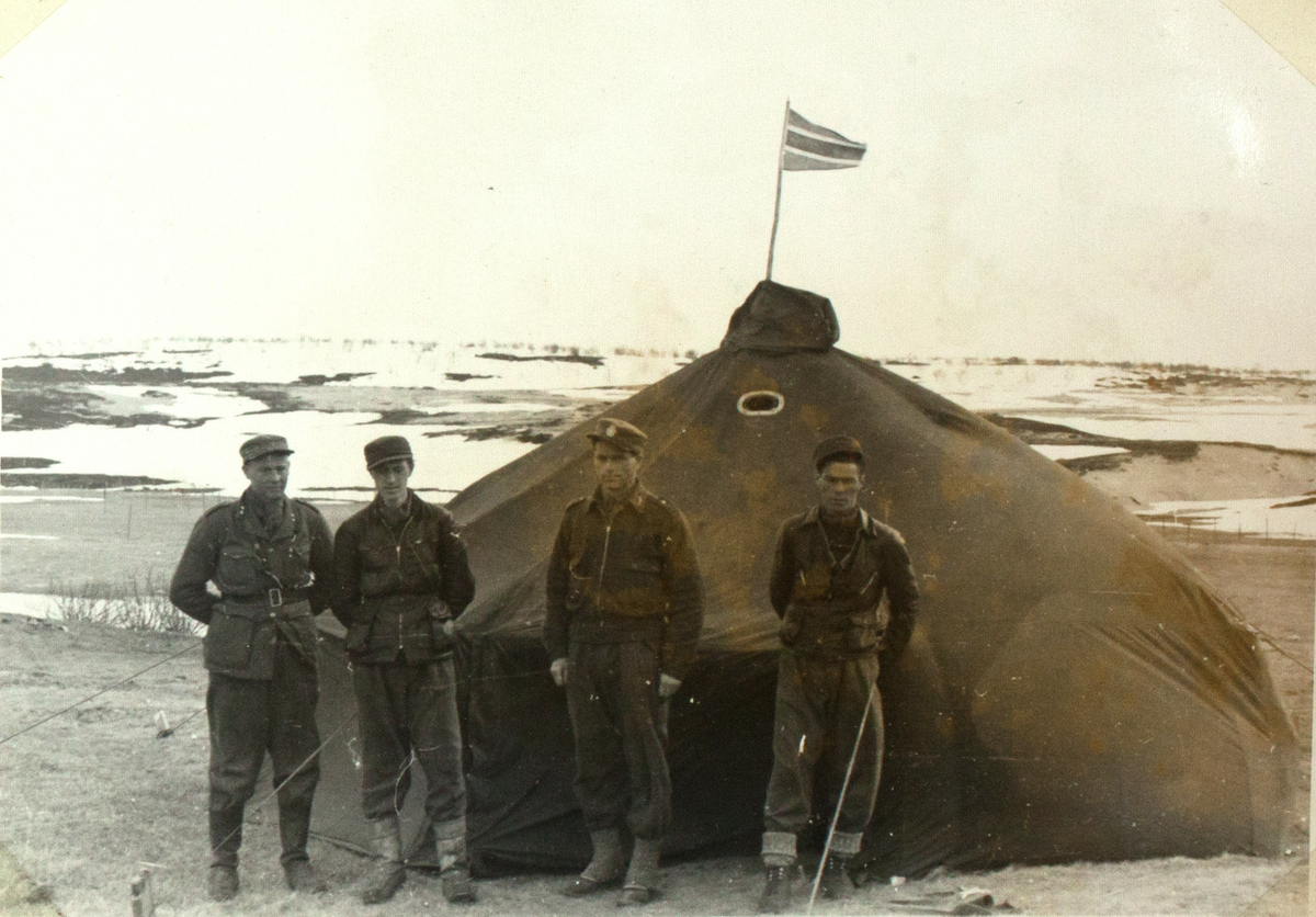 Fire soldater står foran et stort telt. På toppen veiver det et lite, trekantet flagg. I bakgrunnen ser man et delvis snødekket landskap.