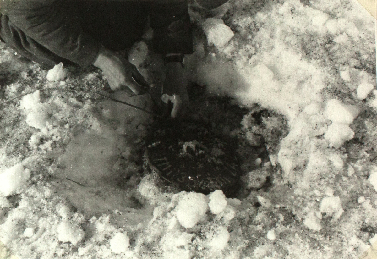På bildet ser man en tallerkenformet landmine som er gravd ned i snøen. En person graver den ut med blotte hender.