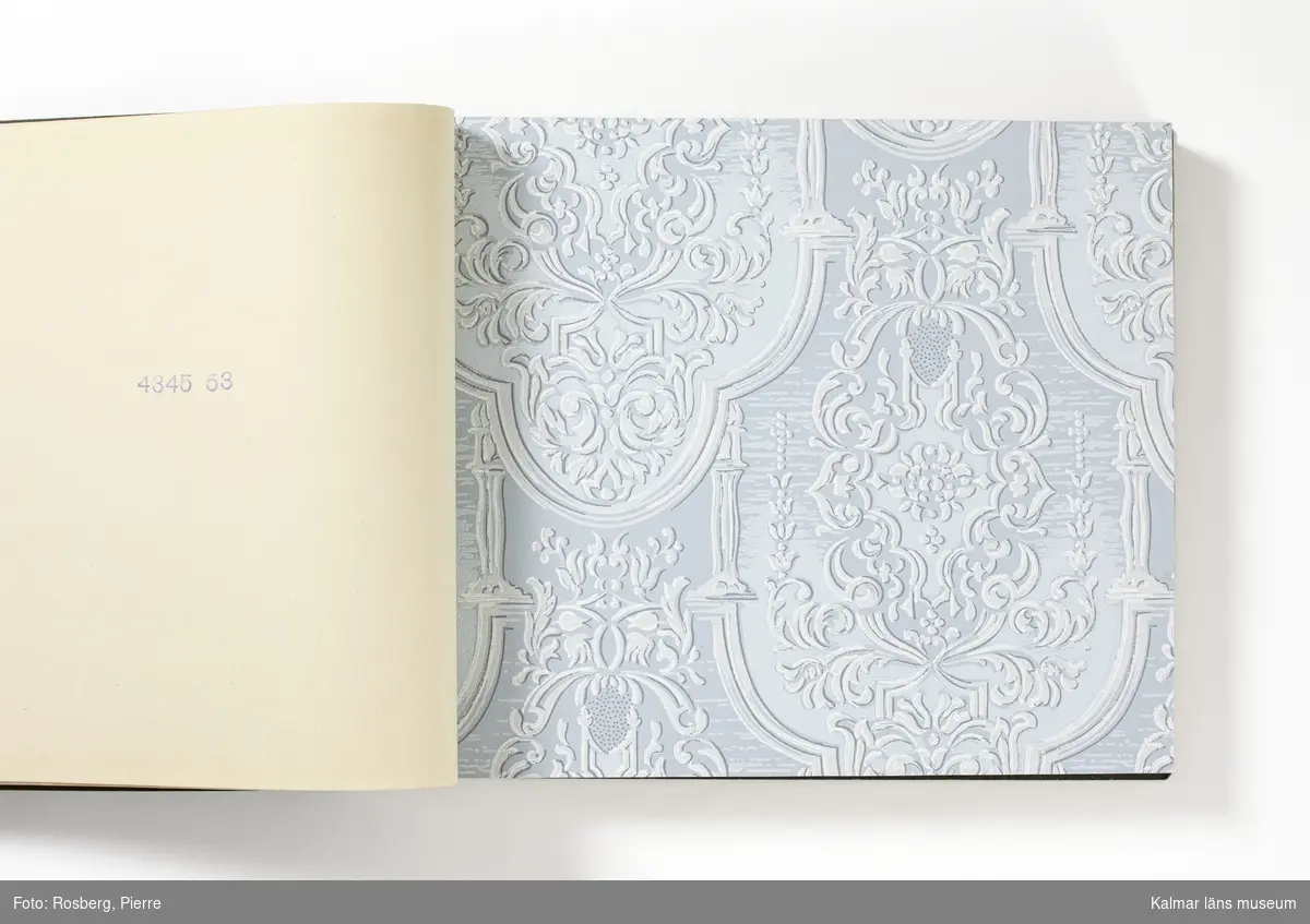 KLM 46599:3. Tapetkatalog. Katalog med pärm av grön papp eller kartong. Bunden med hjälp av tre metallnitar. Text i silver på pärmens framsida: EMMABODA TAPETFABRIK AB Emmaboda. Katalogen innehåller en mängd olika plastförstärkta tapetprover tillverkade av papper, med olika strukturer, färger och mönster, moderna under 1950 och 1960-talen.