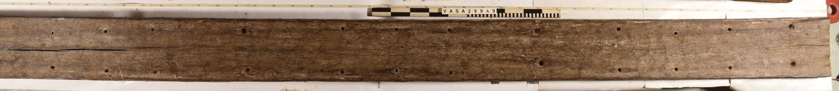 Däcksplanka i ek
Totalt 42 genomgående spikhål, 21 längs plankans ena sida och 21 längs den andra.
Två bulthål uppborrade under bultbytet.
Undersidan är täckt av små sprickor samt har tydliga avtryck från ribbor och däcksbalkar.
Kvarsittande recenta brickor i de flesta spikhål.