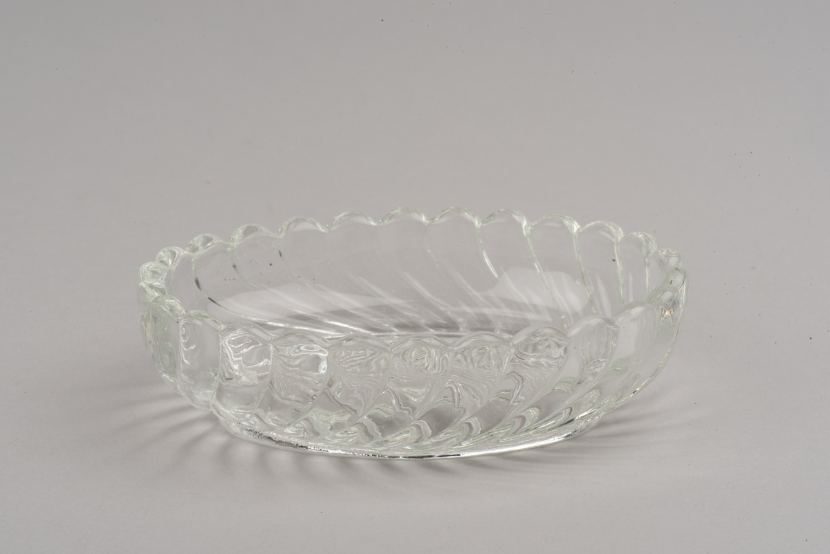 Oval skål av ofärgat glas. Pressad yttäckande dekor i form av spiralvridna åsar som avslutas i en vågformig kant.