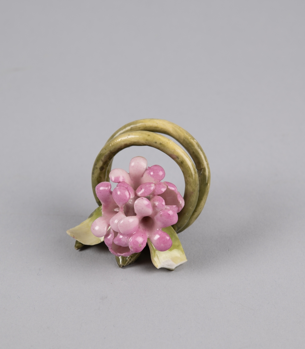 Modellert blomst til borddekor. Stilken danner to ringer som fungerer som en holder til kort eller serviett.
