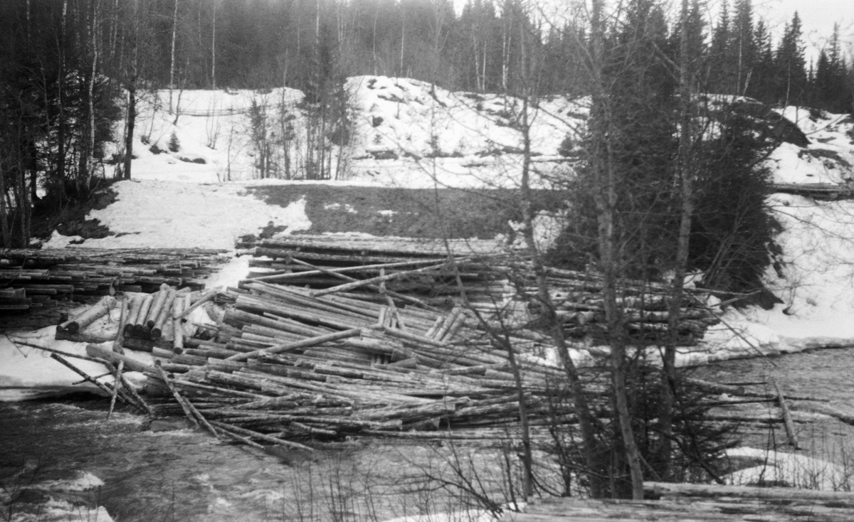 Tømmertillegging ved elva Vismunda i daværende Biri kommune i Oppland i mai 1955. Fotografiet er tatt på tvers av elvefaret, mot en velteplass for fløtingsvirke på motsatt side av elva, Ytterst på denne velteplassen, delvis i et elveløp der det begynte å komme smeltevann med såpass kraftig strøm at noen av stokkene var i ferd med å drive av gårde. Bakenfor og ved sida av lå det strøvelter, der tømmerstokkene lå parallelt i floer - lag - med mellomliggende strøstokker. Med denne luftige tilleggingsmåten fikk tømmeret en forsiktig tørk før fløtingssesongen startet. Dette reduserte faren for at stokkene sank og ble til søkketømmer før det nådde fram til lenseanleggene lengre nede i vassdraget. Det året dette fotografiet ble tatt var det innmeldt 55 583 tømmerstokker til fløting i Vismunda.