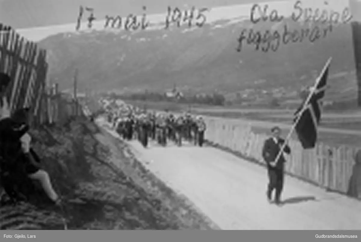 Folketoget på veg frå Skjåk kyrkje 17. mai 1945. 
Ola Sveine (f. 1920) ber flagget framanfor Skjåk Musikklag