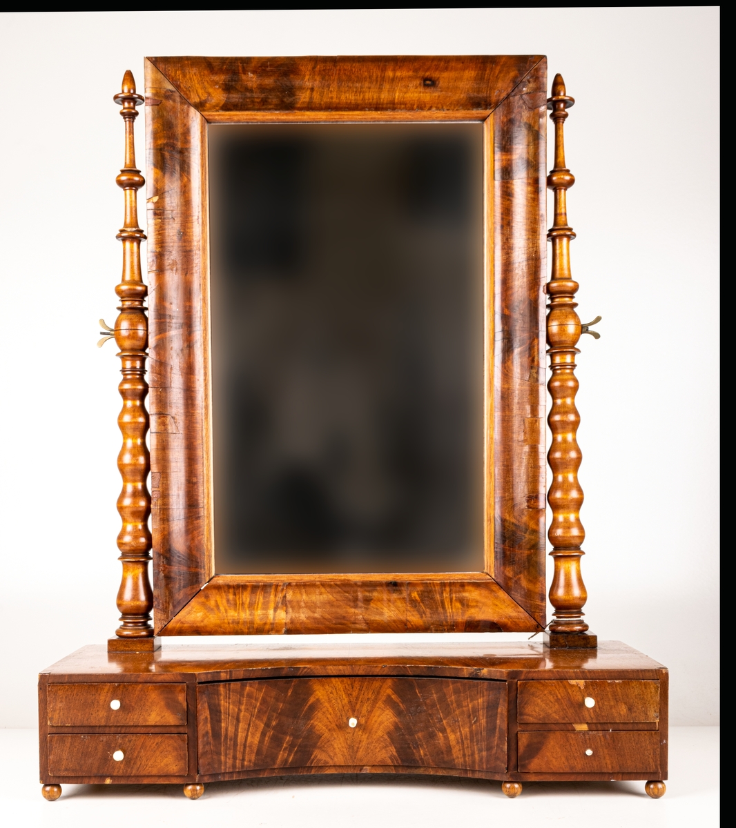 Byråspegel, (lådspegel) av rotmahogny. Med en större och fyra mindre lådor. Svarvade ståndare för spegelns upphängning.