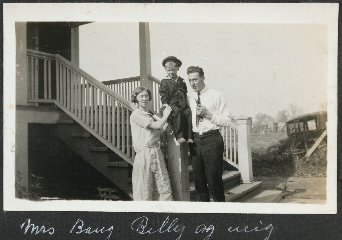 Kvinne og mann med gutt i matrosdress fotografert foran trapp opp til et hus. Til høyre ser man en eldre automobil.