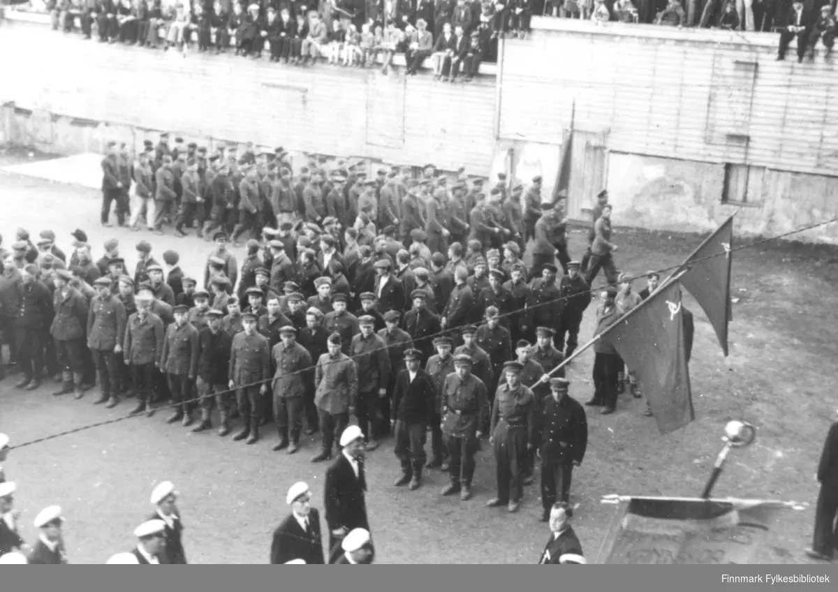 Tidligere russiske krigsfanger oppstilt. Alle i uniform og med russiske flagg. Bildet er tatt 17. mai 1945 i Tromsø.