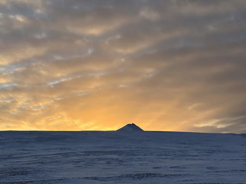 Bildet viser gylden farget himmel med et fjell i forgrunnen. Fjellet heter Trollsteinen og er på Svalbard.
