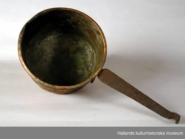 Kastrull av koppar, med skaft och rester av tre avbrutna ben av järn. Rundad botten, nästan cylindriska sidor med rundad mynningskant. Handtaget är platt och avslutat i en krok.