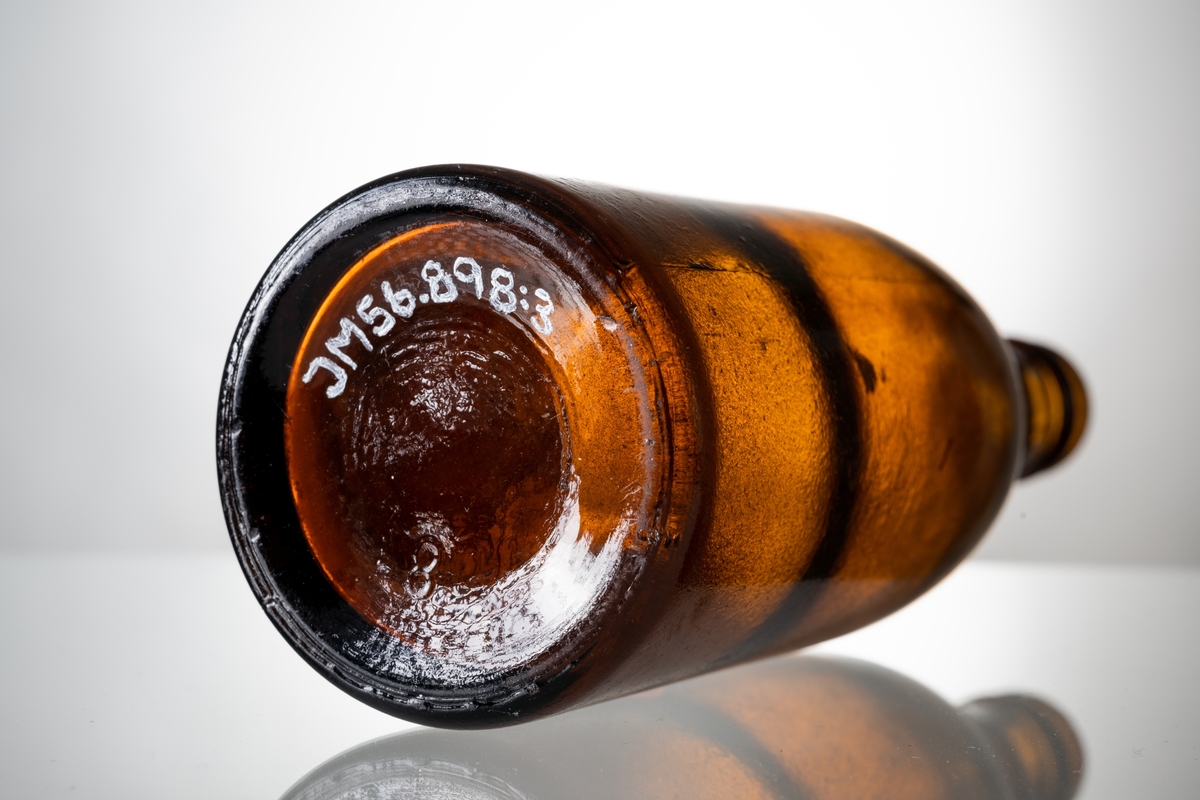 Ölflaskor, 3 st tomma, av brunt glas med påklistrad pappersetikett. Vit etikett med rött och blått tryck, text: "KLASS II KRÖNLEINS Pilsner JÖNKÖPING". På flaskans hals präglat "H" i glaset och tre blomformer (Surte glasbruk). Under botten är präglat siffran 2, 7 respektive 8.

Se vidare Historik.