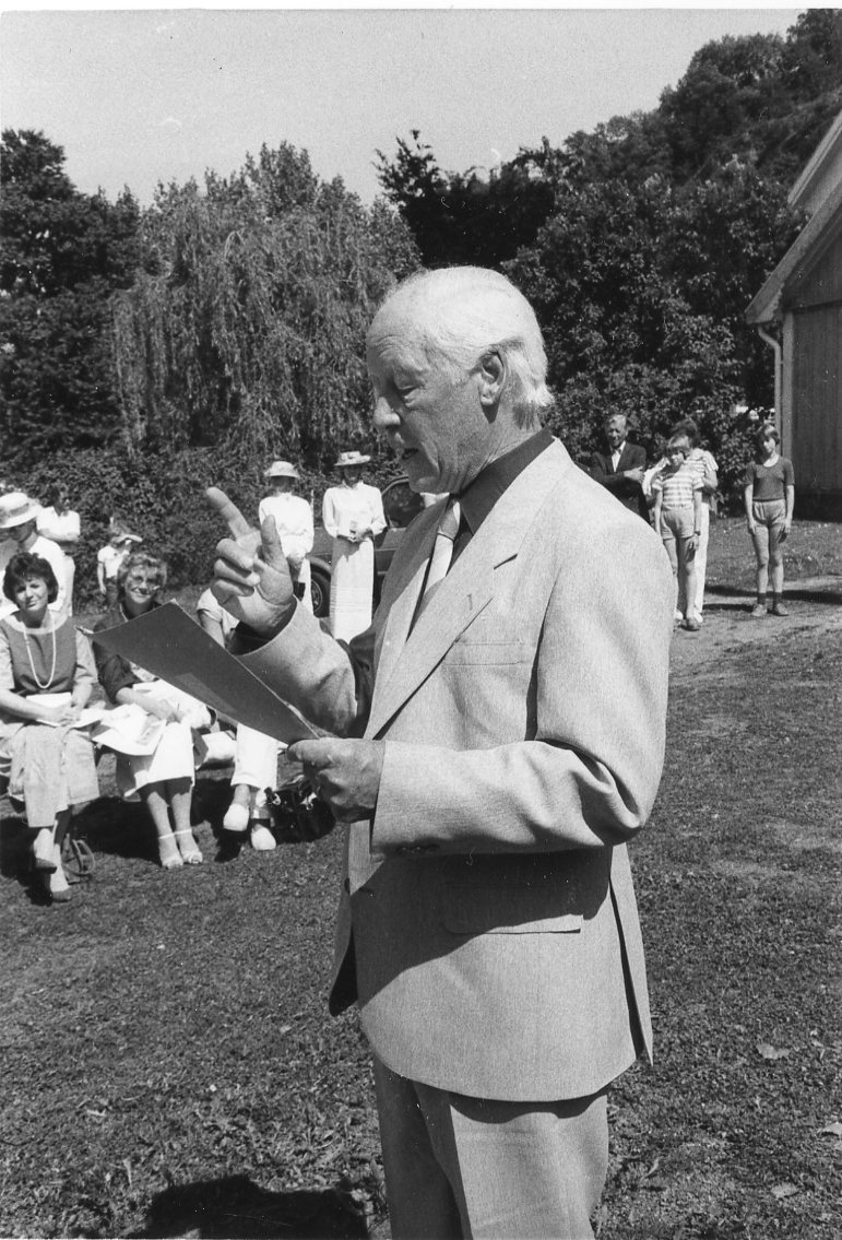 En man står på gården till före detta Grenna pedagogi/småskola och håller ett tal.