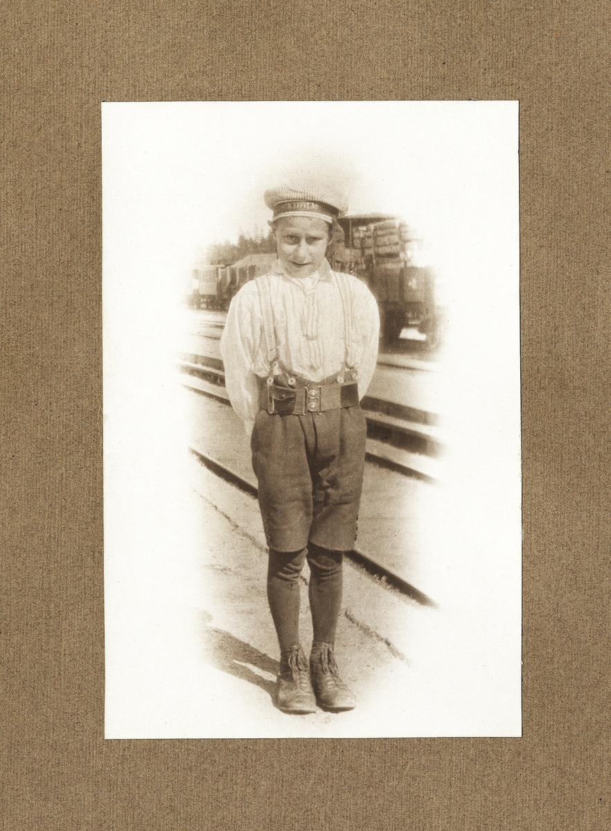 En pojke i kortbyxor och randig sjömansmössa, fotograferad en varm sommardag vid järnvägen.