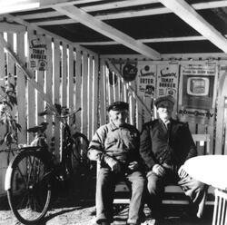 To eldre menn sitter utenfor Skaulund handel i Varteig, på h