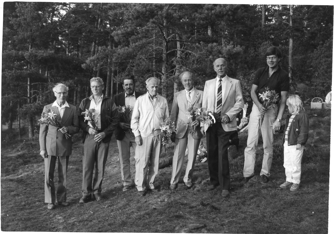 Sju män, och ett barn, på rad med blommor i händerna. De har avtackats som medverkande i uppförandet av en paviljong på Grännaberget.