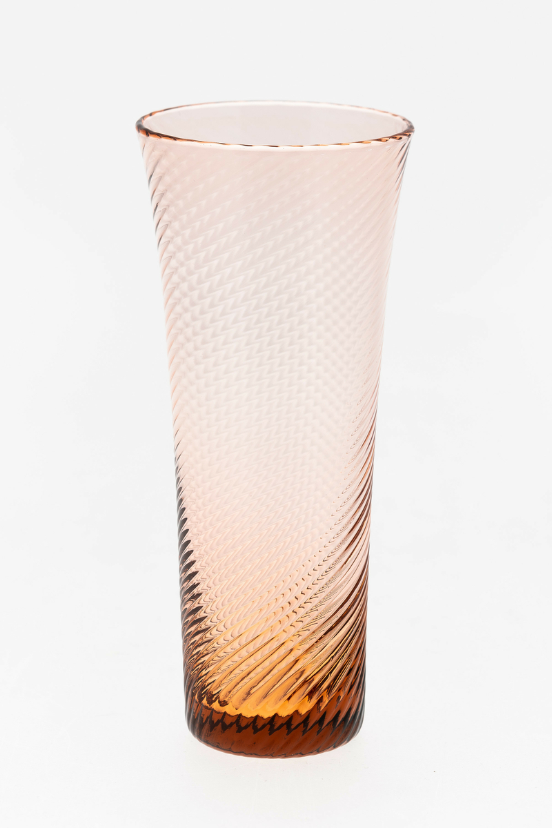 Seltersglass i brunrosa gjennomskinnelig glass. Svak konisk form med sirkulær munningsrand, hvor spiralformede riller snor seg langs korpus.