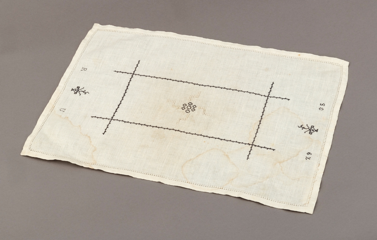 Liten avlang brikke med sort/grått korsstingsbroderi og hvit hullsøm. Påført initialene R.U. på ene kortside og årstallet 1935 på den andre kortsiden.