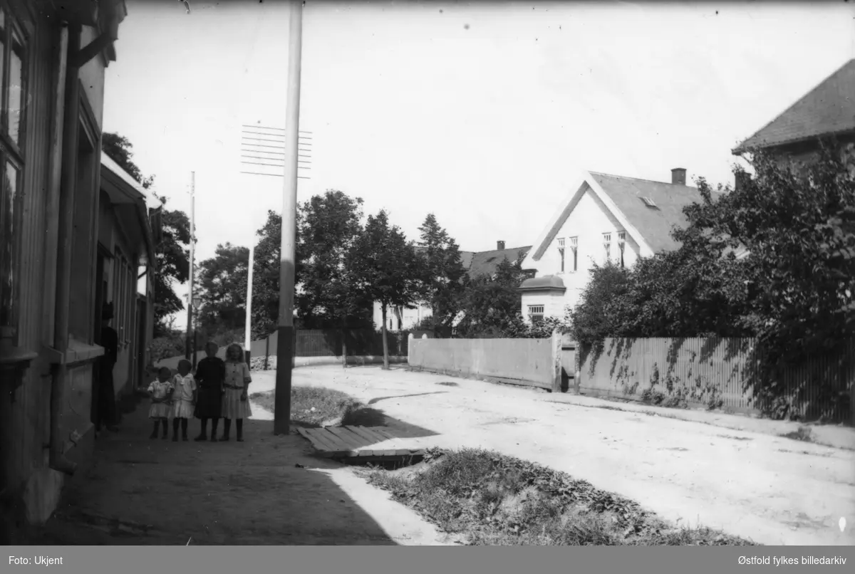 Gateparti fra Høienhaldgata på Jeløy, Moss ca. 1920. Fire ukjente barn. Bakerste huset (skimtes) er huset til dr. Nyquist på hjørnet Høienhaldgata - Løkkegata. Ukjent kvinne i porten.
