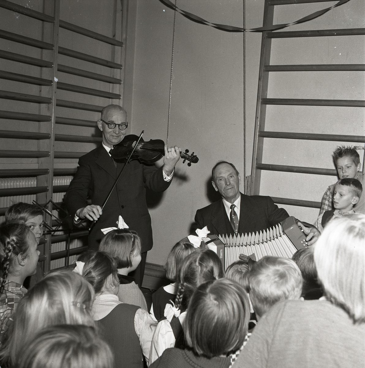 Två spelmän spelar inför publik vid gymnastikfest i Lottefors, januari 1956.