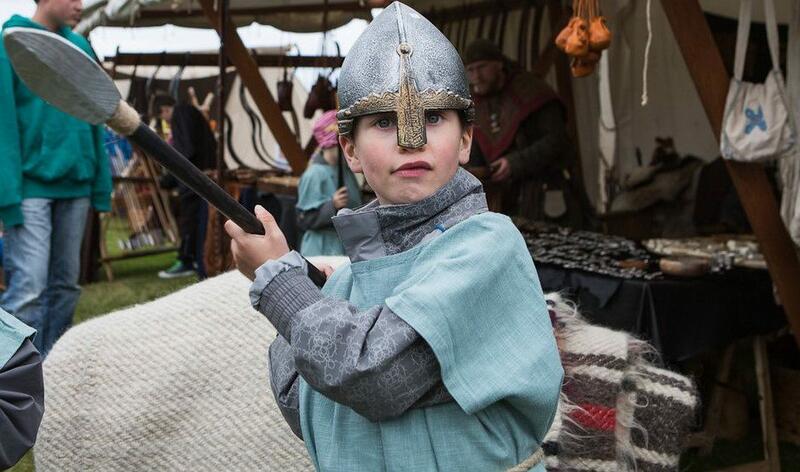 Et barn i vikingklær og hjelm holder et spyd