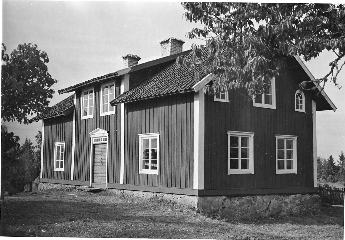 En hus med locklistpanel, vita knutar och fönsteromfattningar samt frontespis.