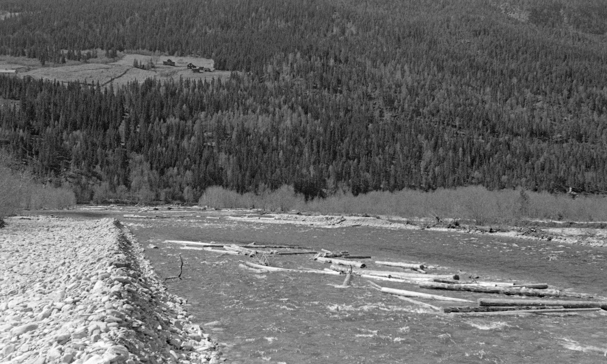 Fra sideelva Vålas utløp i Gudbrandsdalslågen, like sørvest for kommunesenteret i Ringebu i Midt-Gudbrandsdalen. Fotografiet ble tatt i 1957, på et tidspunkt da det nettopp var gjort såkalte «elveforbedringsarbeider» i denne delen av Våla. Her hadde man ved hjelp av bulldoser skjøvet mye av steinen fra den sentrale delen av elvefaret opp på en av elvebreddene. Dette ble gjort for at fløtingstømmeret i Våla skulle flyte lettere ned mot Lågen. Da dette fotografiet ble tatt lå det likevel en del stokker på noen ører i elveløpet, men forholdene for fløtinga var likevel forbedret. I den nordøstvendte lia på motsatt side av dalføret ser vi småbruket Rydningen.