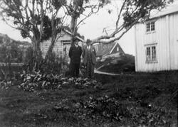 Amatørportrett av to menn stående i en hage. I bakgrunnen bo