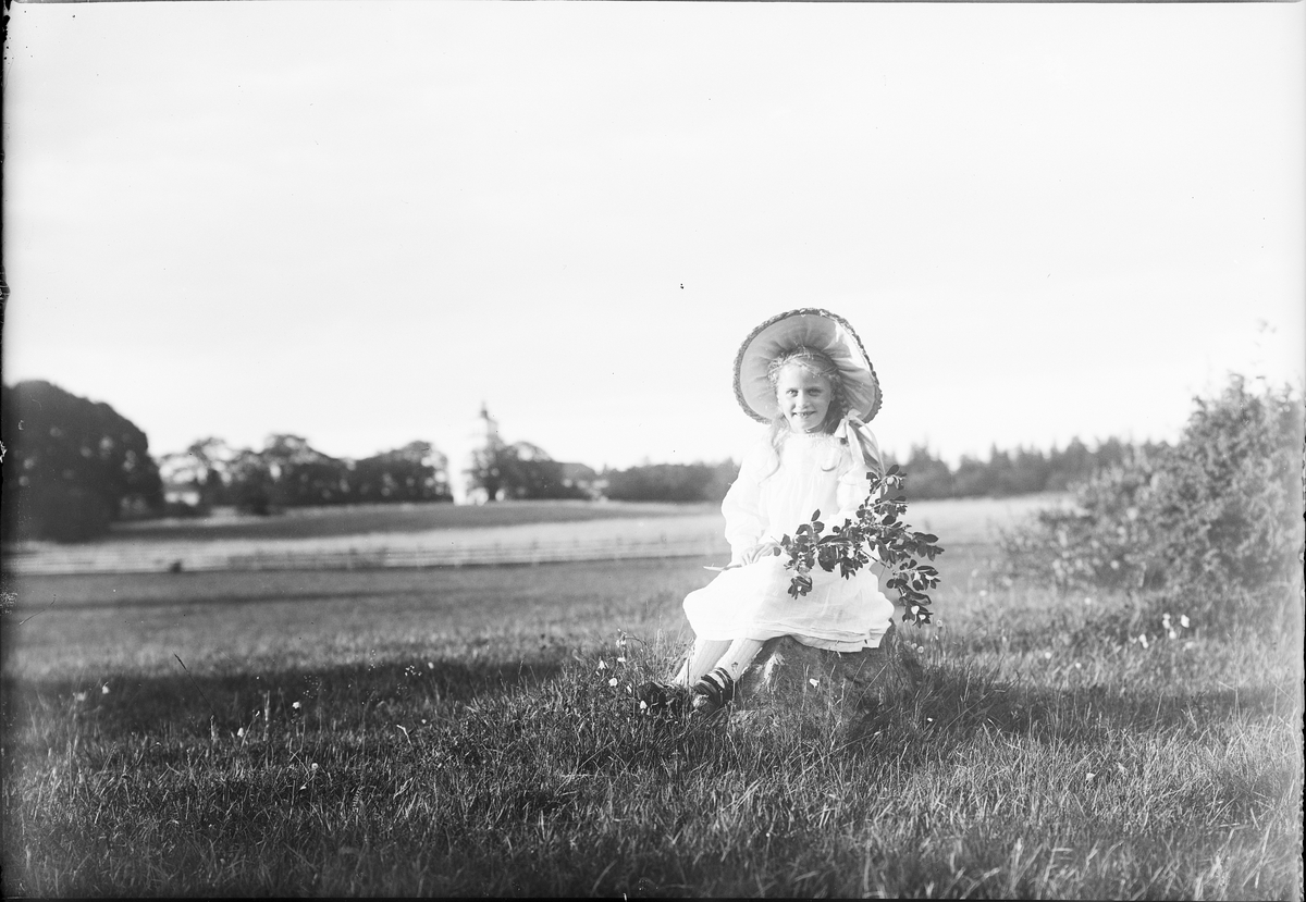 Flicka sitter på en sten med en kvist i handen, Östhammar, Uppland