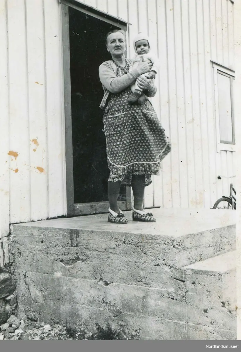 Aminda Birgitte Johansen (f. 1889) fotografert på trappa heime på Sund med barnebarnet Jann-Viggo på armen.
